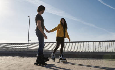 Happy young couple holding hands while skating on pier - VEGF03526