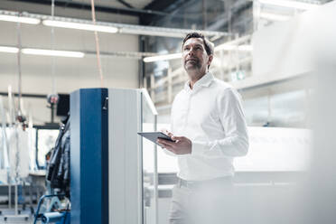 Male inspector with digital tablet examining equipment while standing at industry - JOSEF03032