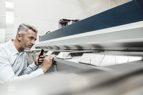 Mature inspector examining machine while standing at industry stock photo