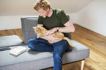 Man looking at cat while sitting on couch in living room - MEF00060