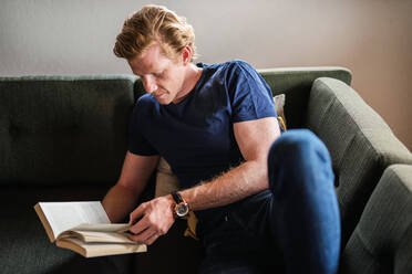 Man reading book while sitting on sofa at home - MEF00064