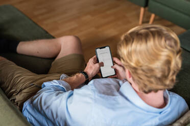 Man text messaging on mobile phone while lying on couch in living room - MEF00076