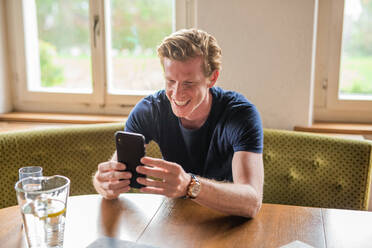 Happy man doing video call on smart phone in living room - MEF00078