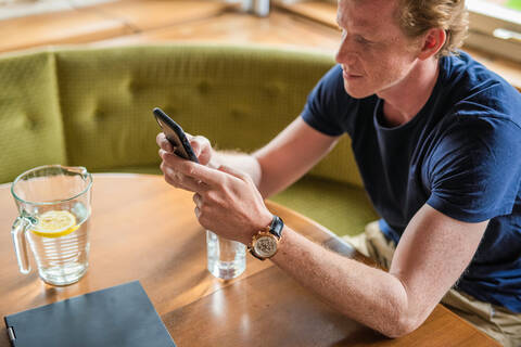 Mid adult man text messaging on mobile phone in living room stock photo