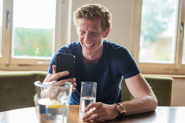 Man laughing while on video call through smart phone in living room - MEF00082