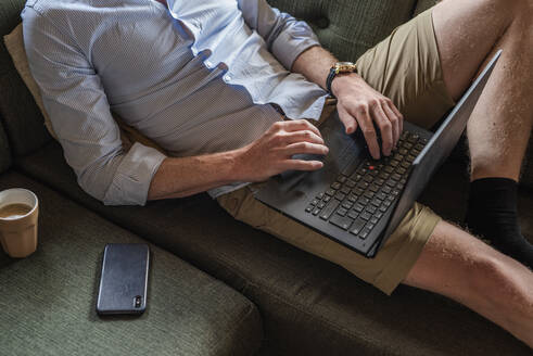 Mann bindet Laptop um, während er zu Hause auf der Couch sitzt - MEF00084