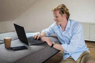 Smiling businessman working on laptop at home - MEF00088