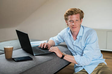 Male entrepreneur with laptop by couch in living room - MEF00090