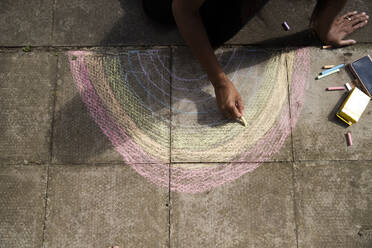 Arme einer erwachsenen Frau, die mit Buntstift einen Regenbogen auf dem Bürgersteig zeichnet - PMF01698