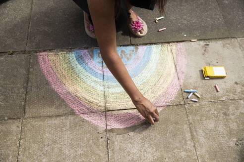Arm einer erwachsenen Frau, die mit Buntstift einen Regenbogen auf den Bürgersteig zeichnet - PMF01699