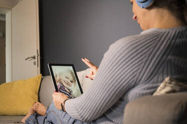 Mother and daughter on video call through digital tablet at home - UUF22394