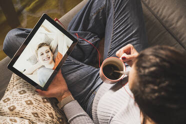 Ältere Frau hält Kaffeetasse während Videoanruf auf digitalem Tablet zu Hause - UUF22399