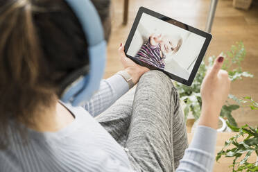 Mother showing thumbs up to daughter on video call through digital tablet - UUF22405