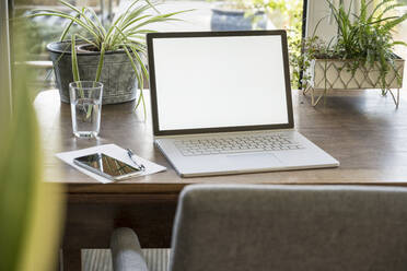 White device screen of laptop by glass on table at home - UUF22426