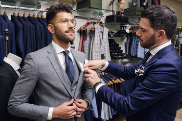 Tailor in his menswear store adjusting handkerchief in customers suit pocket - AODF00173