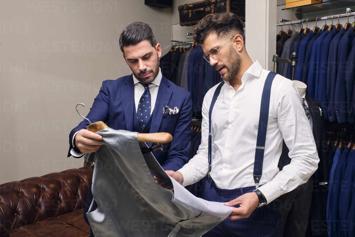 Tailor and customer looking at gray waistcoat in tailors boutique