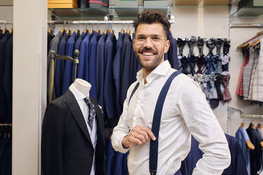 Porträt eines lächelnden Mannes in weißem Hemd und blauen Hosenträgern in einem Schneiderladen - AODF00187