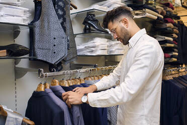 Customer browsing shirts on rack in tailors boutique - AODF00199