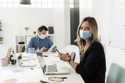 Geschäftsleute mit Schutzmasken bei der Arbeit im Büro - GIOF10425