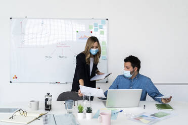 Geschäftsleute mit Schutzmasken bei der Arbeit im Büro - GIOF10429