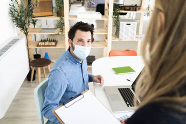 Business people wearing protective masks talking in office  - GIOF10433