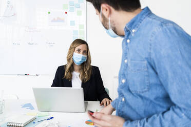 Geschäftsleute mit Schutzmasken bei der Arbeit im Büro - GIOF10437