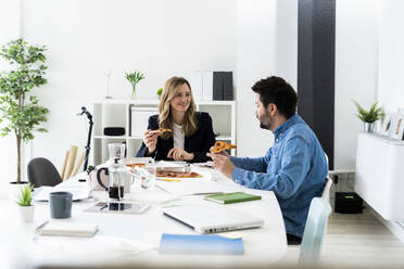 Geschäftsleute, die in der Pause Pizza essen und sich im Büro unterhalten - GIOF10459