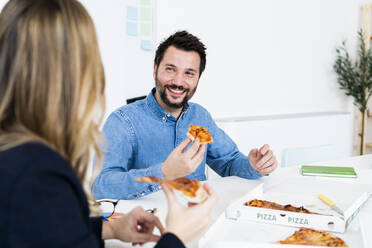 Geschäftsleute, die in der Pause Pizza essen und sich im Büro unterhalten - GIOF10461