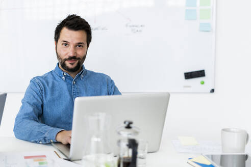 Portrait of smiling man using laptop in office - GIOF10480