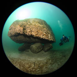 Fischaugenansicht eines Tauchers, der an einem Gletscherstein im Attersee vorbeischwimmt - YRF00264