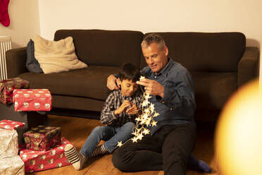 Father and son with illuminated Christmas lights sitting in living room - PMF01722