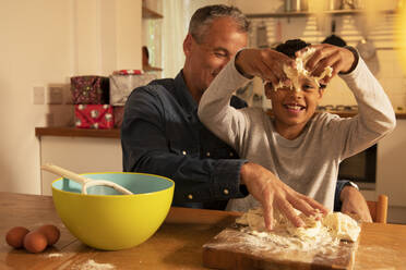 Father and son kneading dough on table while sitting in kitchen - PMF01726