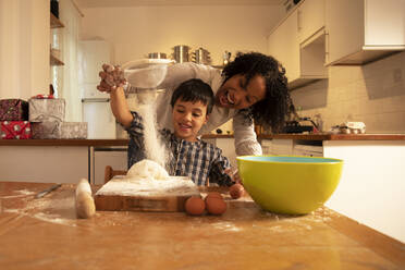 Cheerful mother screaming while mixing ingredients with son on table in kitchen - PMF01727