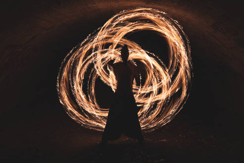Young man performing fire ring skill in dark tunnel - JAQF00154