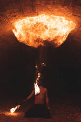 Junger Mann mit Feuerstab jongliert in dunklem Tunnel - JAQF00159