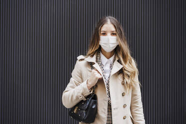 Mid adult woman with purse wearing protective face mask against black wall - EBBF02084