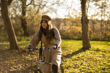 Modische Frau sitzt auf einem Fahrrad in einem öffentlichen Park - AXHF00026