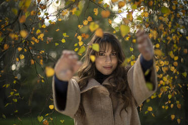 Smiling woman holding branch while standing in park during autumn - AXHF00039