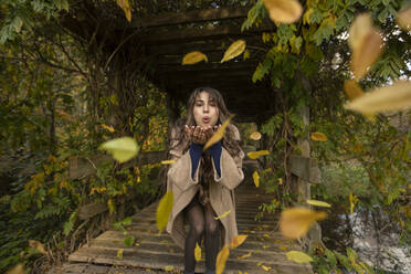 Cheerful woman blowing autumn leafs in public park - AXHF00046