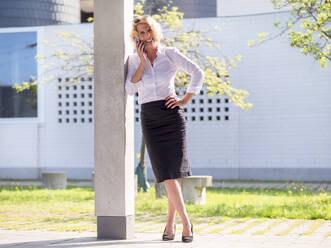 Smiling businesswoman talking over smart phone while standing by column - LAF02623