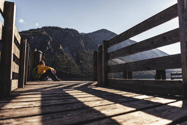 Mature male hiker sitting on pier against mountain - UUF22430