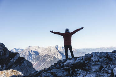 Unbeschwerter männlicher Wanderer mit ausgestreckten Armen auf einem Berg stehend gegen den klaren Himmel im Winter - UUF22435