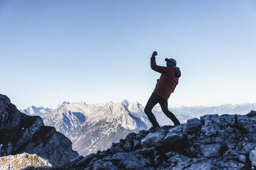 Carefree mature man dancing on mountain against clear sky during winter - UUF22436