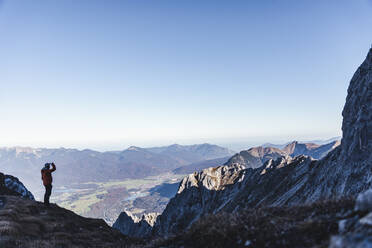 Männlicher Wanderer, der die Aussicht betrachtet, während er auf einem Berg gegen den klaren Himmel steht - UUF22437