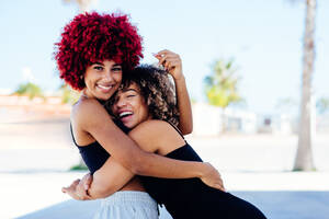 Zwei attraktive Latino-Mädchen mit Afro-Haar, die sich freundschaftlich umarmen. - CAVF91576
