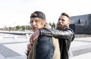 Man with hand on boyfriend's shoulder walking on street against clear sky - JCCMF00662