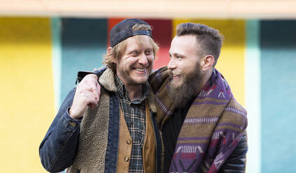 Smiling gay boyfriends standing against colorful wall - JCCMF00671