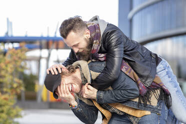 Playful boyfriend piggybacking gay man while standing in city - JCCMF00678