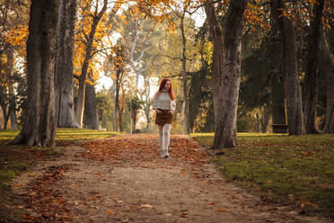 Mittlere erwachsene Frau, die im Herbst auf einem Fußweg im Park spazieren geht - MRRF00764