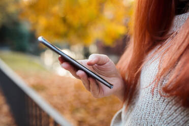 Nahaufnahme einer Frau im mittleren Erwachsenenalter, die im Park ein Mobiltelefon benutzt - MRRF00768